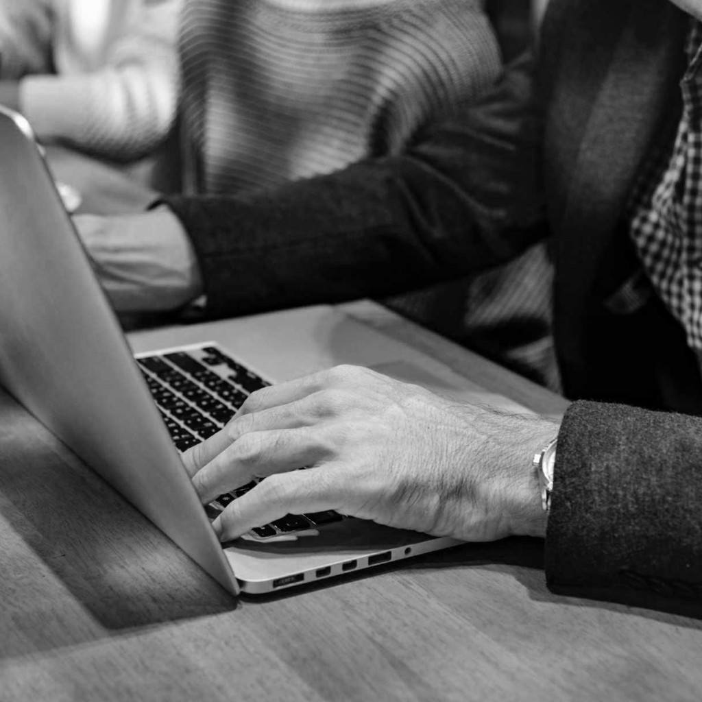 neck down shot of man sitting at wooden desk with open laptop