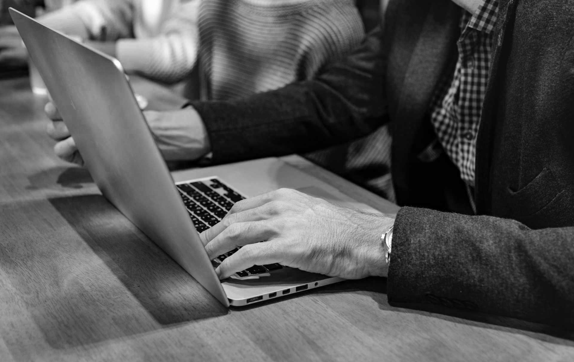 neck down shot of man sitting at wooden desk with open laptop