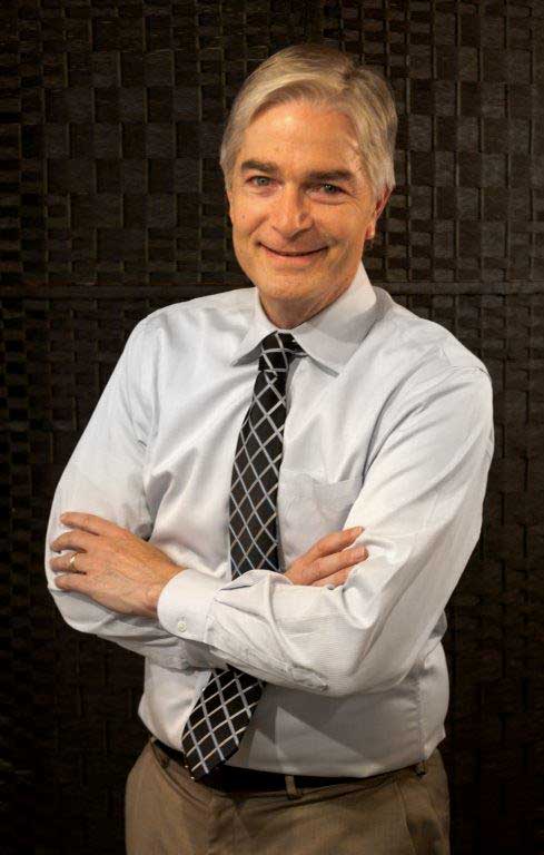 smiling man with gray hair wearing white shirt and crosshatched black and silver tie with his arms crossed