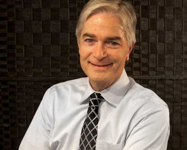 smiling man with gray hair wearing white shirt and crosshatched black and silver tie with his arms crossed