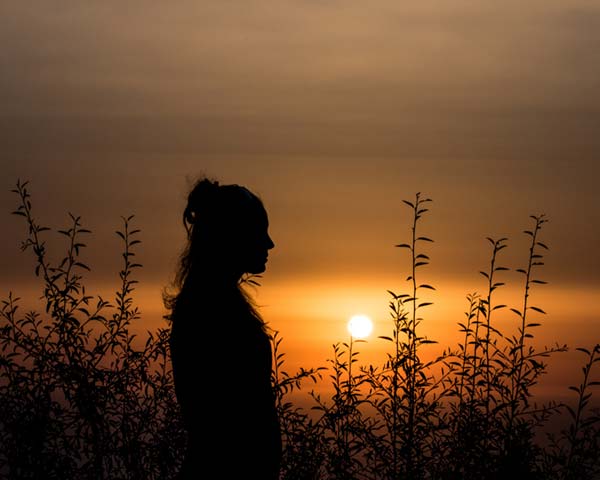 profile silhouette of native man standing in front of bushes at sunset